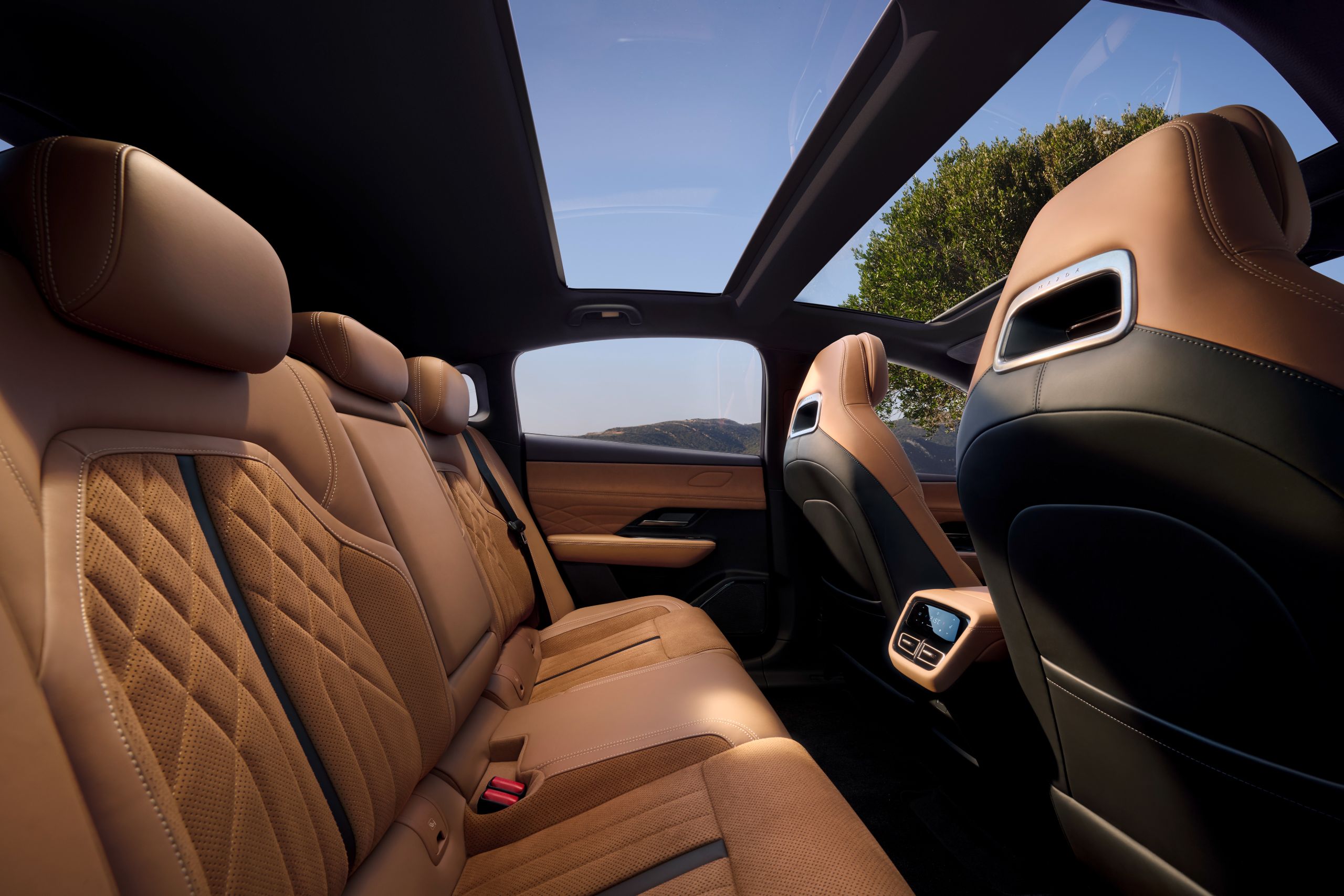 Rücksitzbereich des Mazda 6e mit brauner Lederausstattung, Panoramadach und edlem Interieur-Design vor Berglandschaft im Hintergrund.