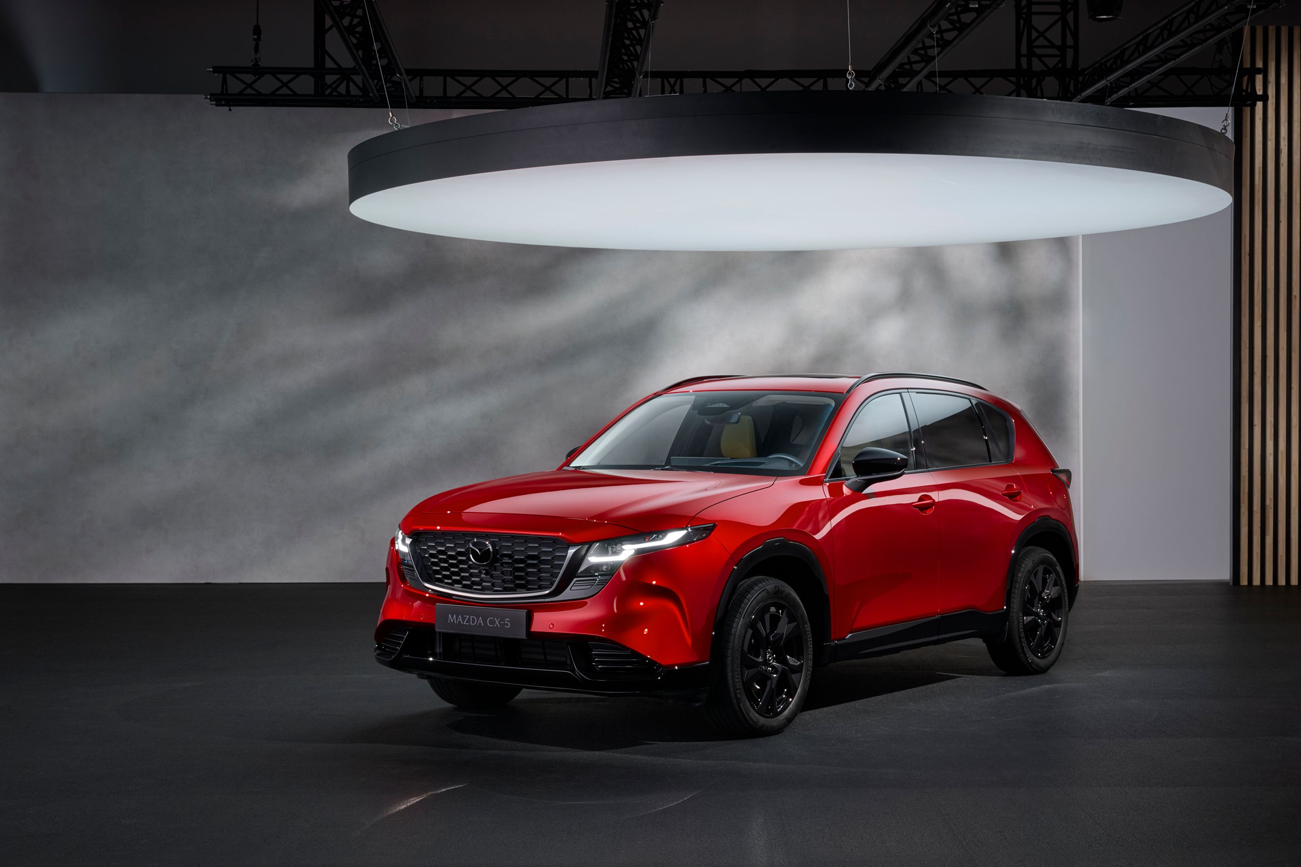 Mazda CX-5 2025 in der Farbe Soul Red Crystal in einem modernen Showroom mit indirekter Beleuchtung – sportliches SUV mit schwarzem Kühlergrill und schwarzen Felgen.